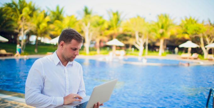 Image of young man working on a computer near a pool.