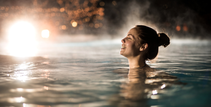 A woman enjoying a relaxing swim in a heated pool at night, powered by the NCS Premier Series Heat Pump.